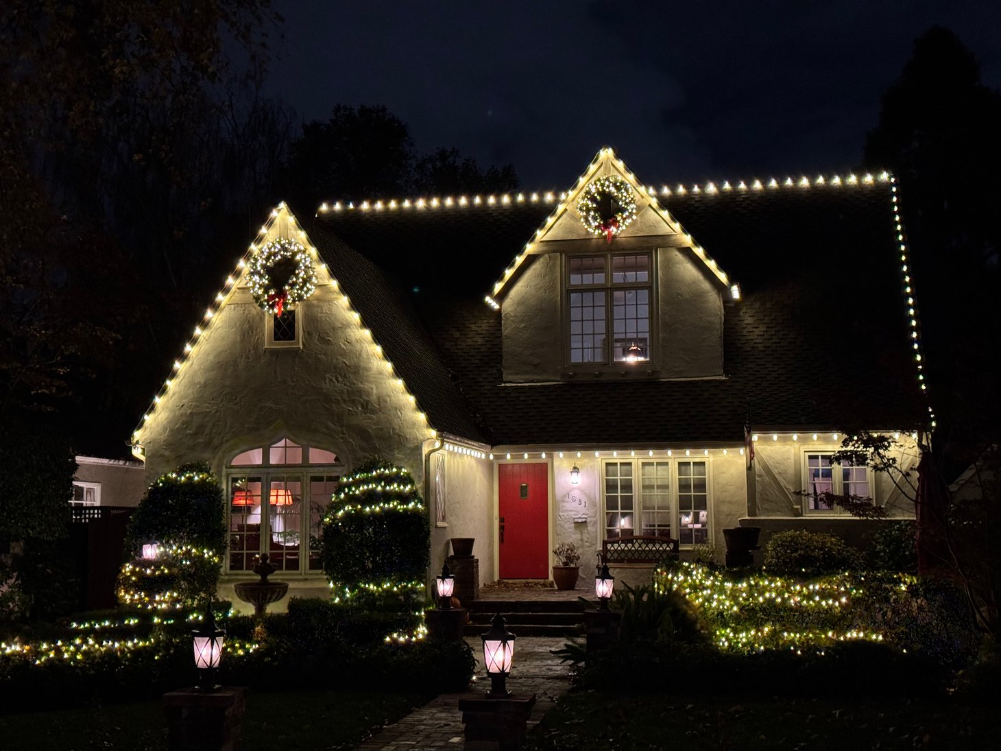 Warm white Christmas lights trace the roofline and gables of a home at night.