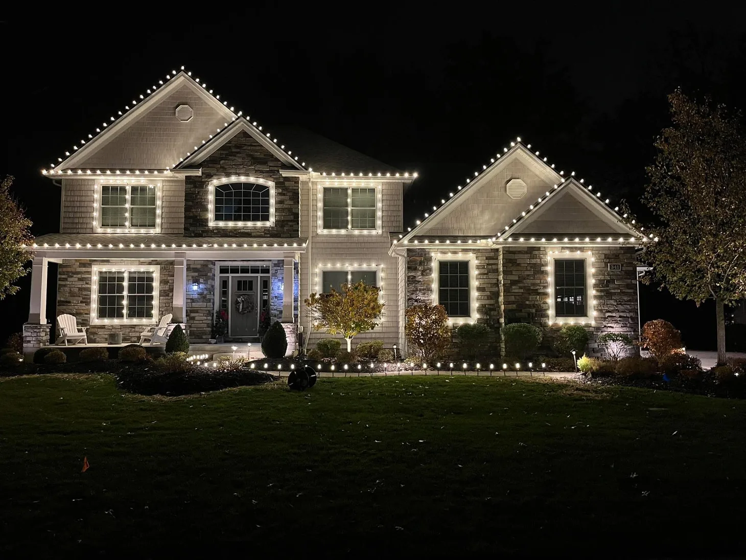 Two-story home outlined with warm white Christmas lights along the roof and windows.