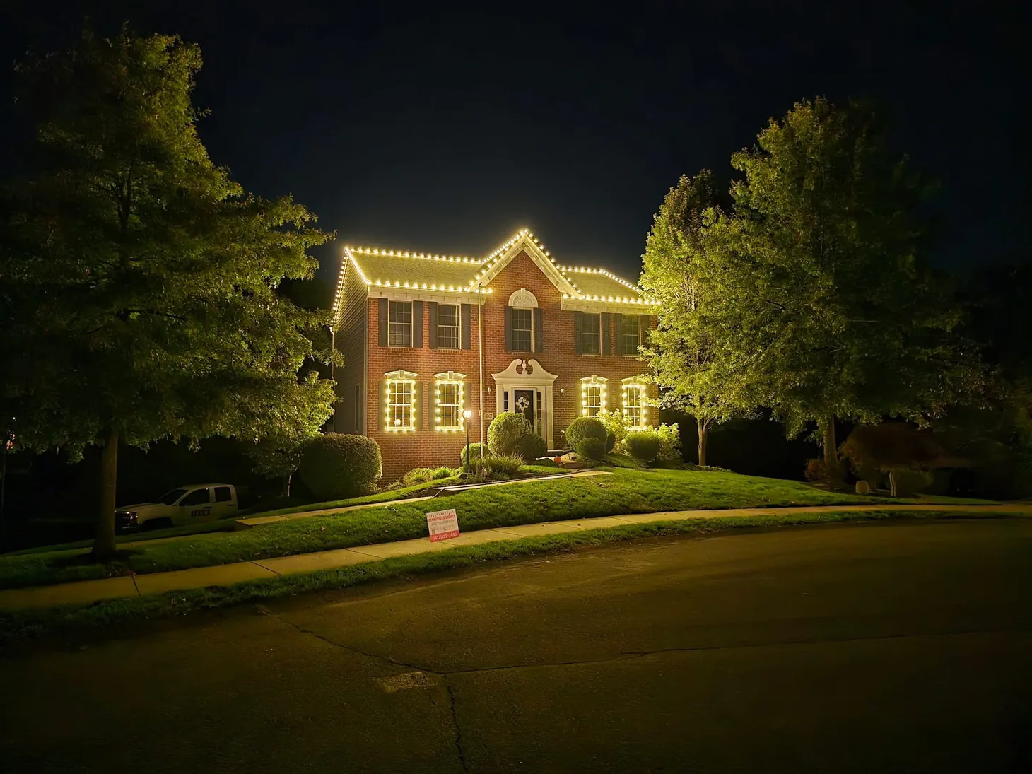 Home decorated with Christmas roofline lights, framed by trees at night.