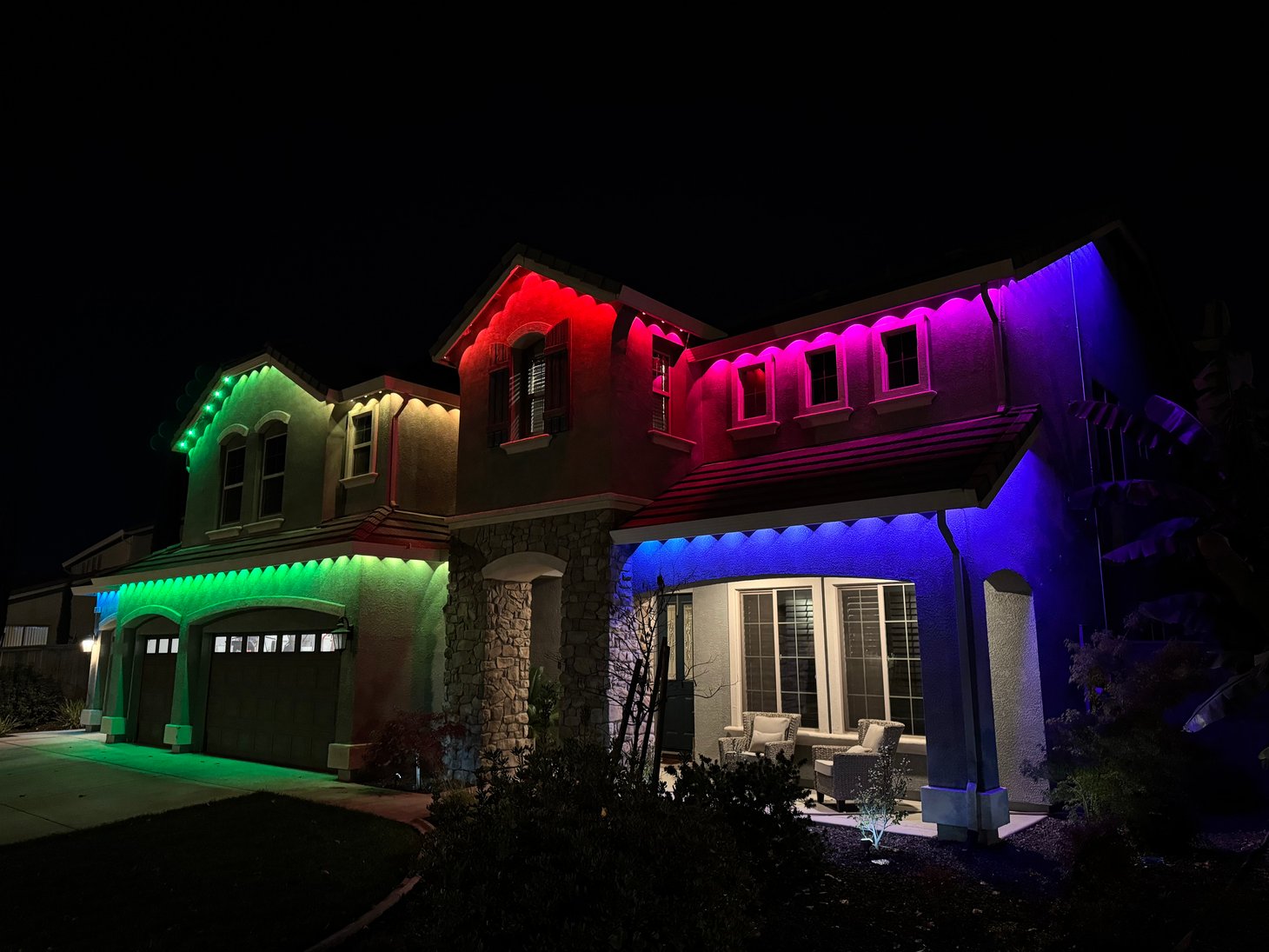 Two-story home illuminated with multicolor permanent lights along the roofline.